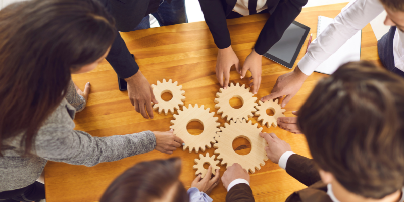 A group of people holding wooden gears around a table.