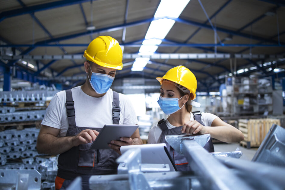 Industrial workers with face masks protected against corona virus discussing about production in factory.