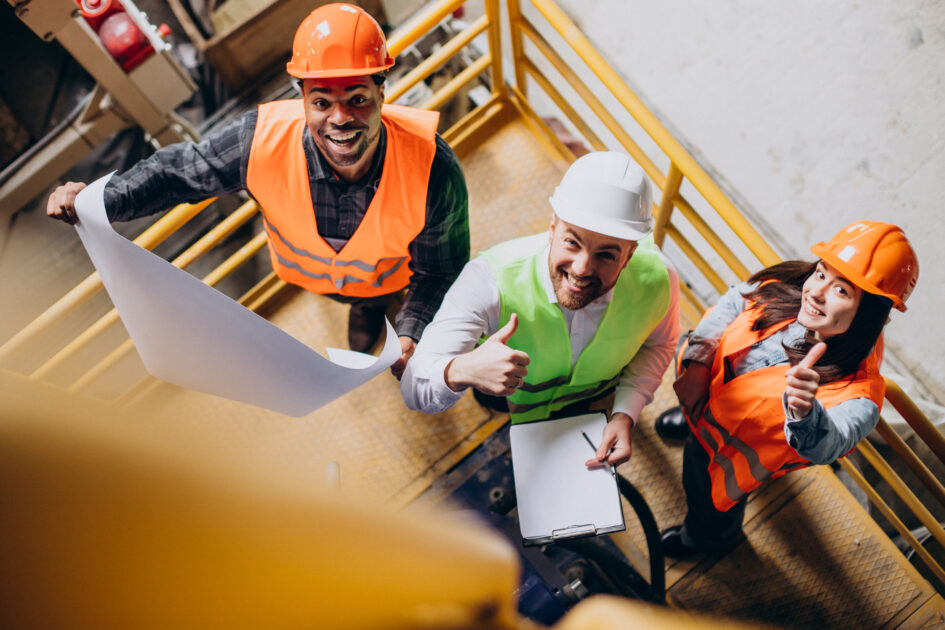 Three factory workers in safety hats discussing manufacture plan