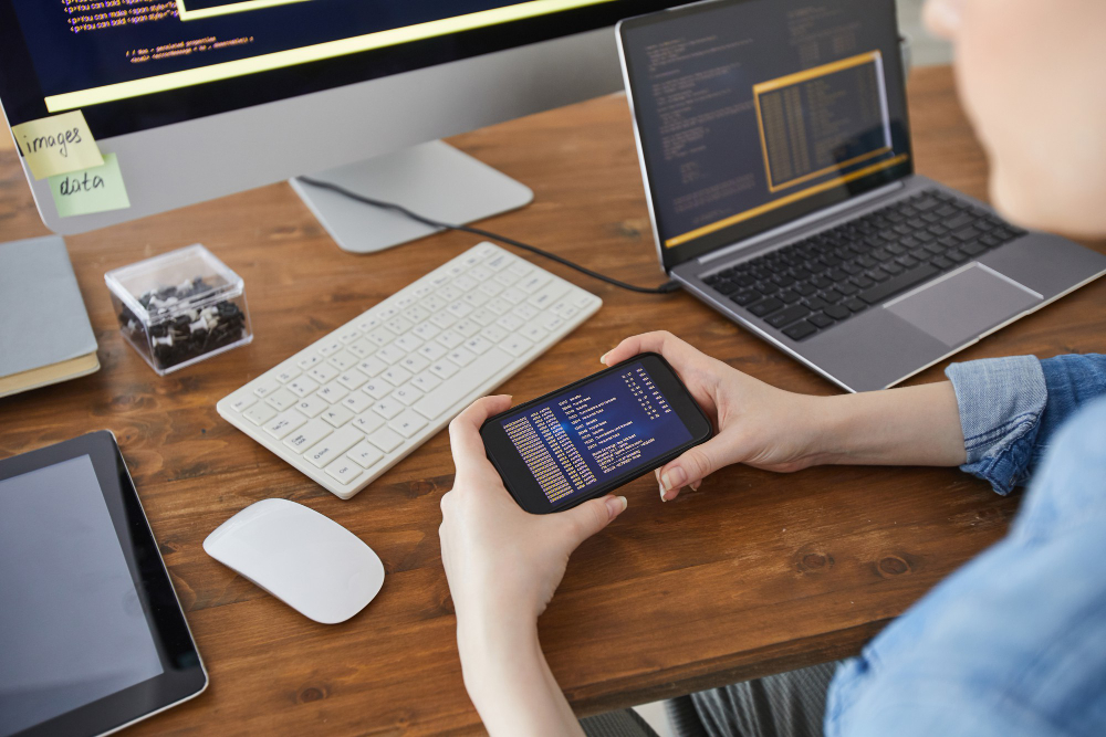 A woman utilizing an Android emulator on her cell phone while seated at a desk.