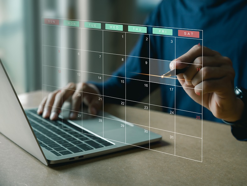 A man is using a laptop with a calendar on it.