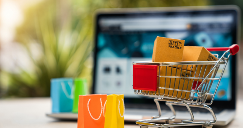 A shopping cart, laptop and coupon platform sit on a table.