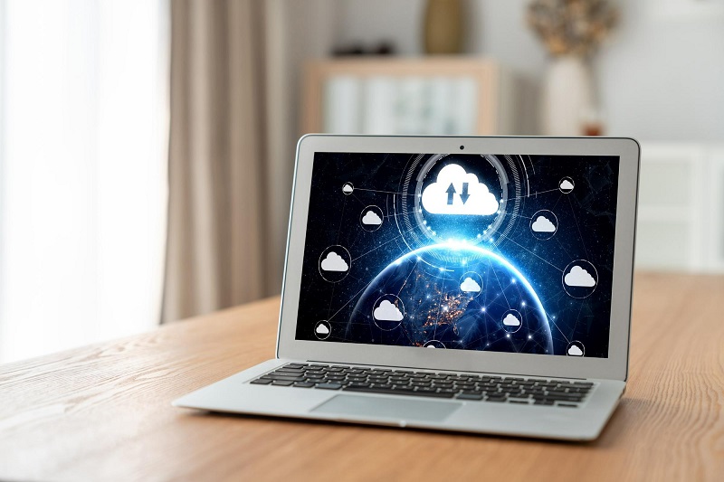 A laptop with a cloud on it sitting on a wooden table.