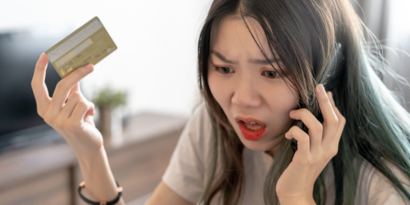 A woman engaging in complaint management systems while holding a credit card and talking on the phone.