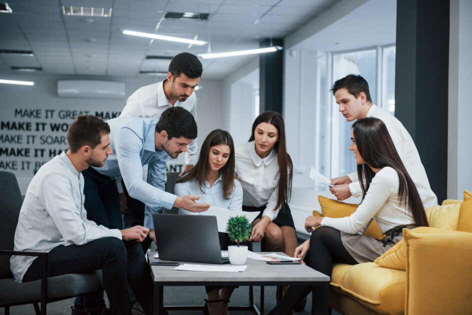 Guy shows document to a girl. Group of young freelancers in the office have conversation and working