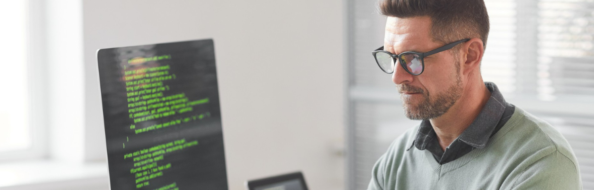 A man in glasses is using Android emulators to view code on a computer screen.