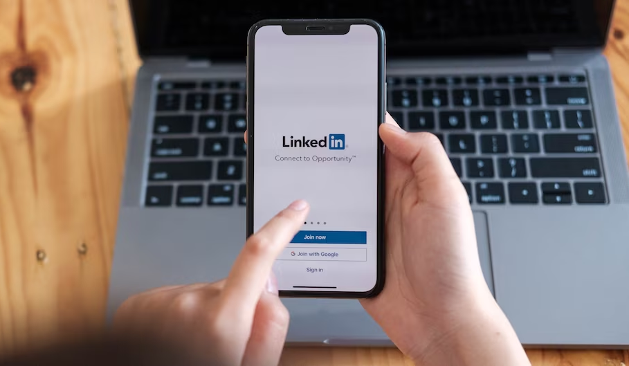 A woman holding a phone with the linkedin logo on it.