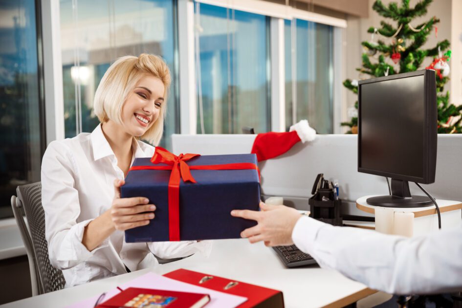 Colleagues celebrating christmas party in office smiling giving presents.