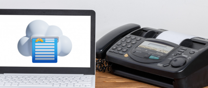 A laptop with an online fax service next to a wooden table.