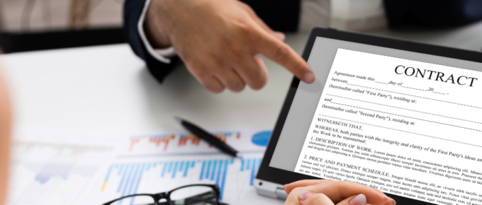 A person is pointing at a contract on a laptop during a business meeting.