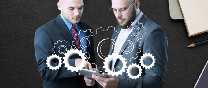 Two businessmen are looking at a tablet with gears on it.