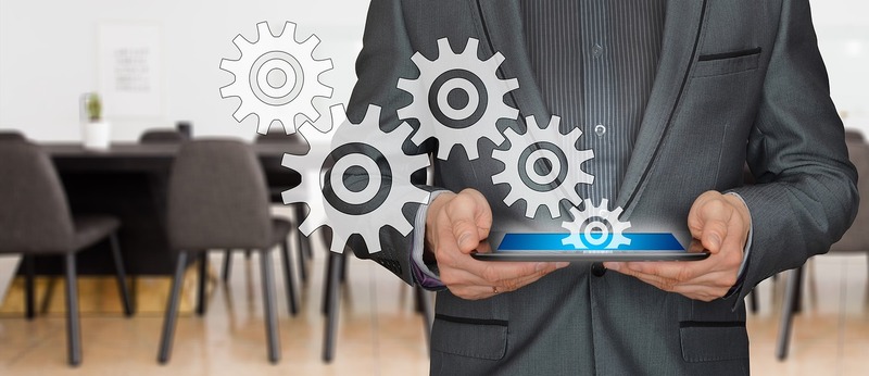 A businessman holding up a tablet with gears on it.