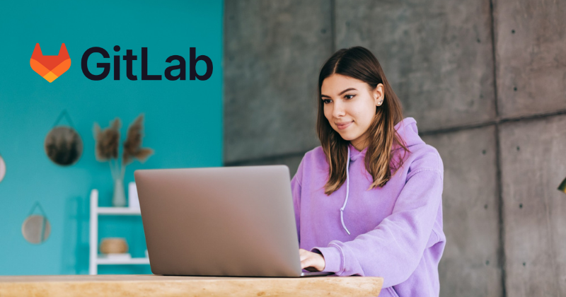 A woman is working on a laptop with the gitlab logo.