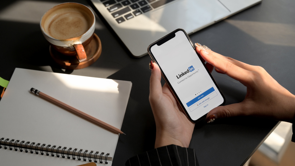 A woman holding a phone with the linkedin logo on it.