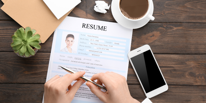 A person using LinkedIn summary generators while writing a resume on a desk with a cup of coffee.