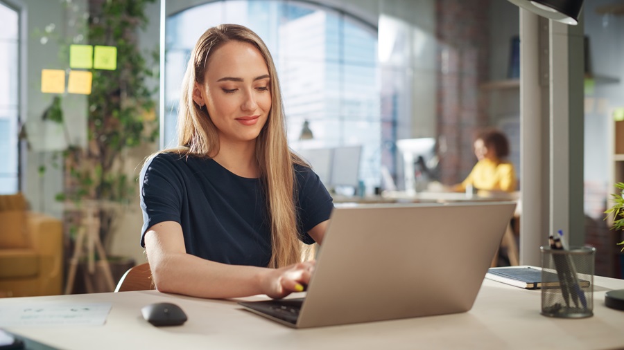 Beautiful Female in a Black Casual Dress Sitting at a Desk in Creative Office, Working on Tasks on Laptop Computer. Young Creative Specialist Writing Corporate Project Plans for Marketing Agenda.